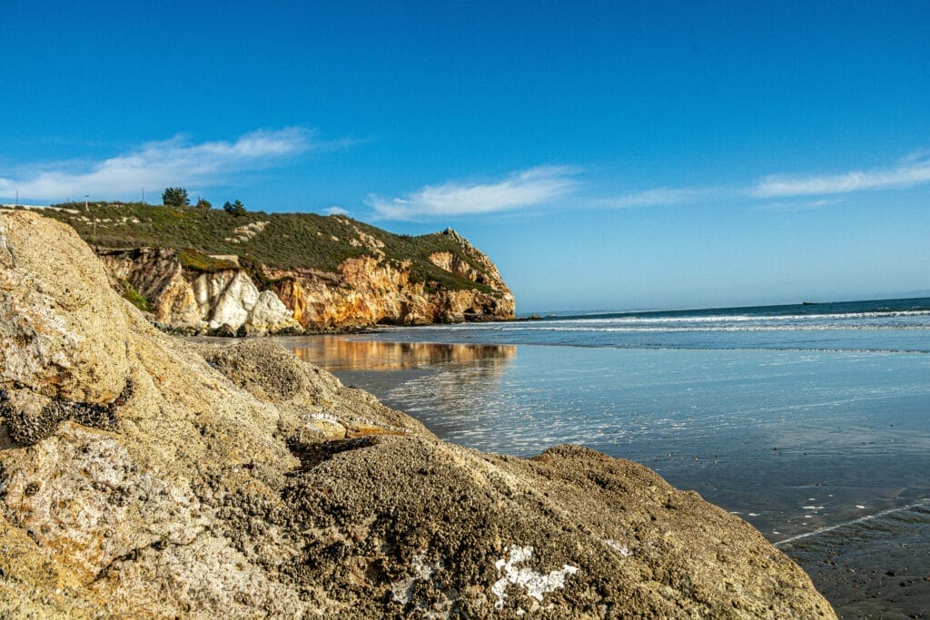 A man is sitting on a rock on a Morro Bay beach.