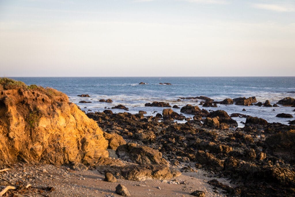 A person is standing on a rocky beach near the ocean along the central coast.
