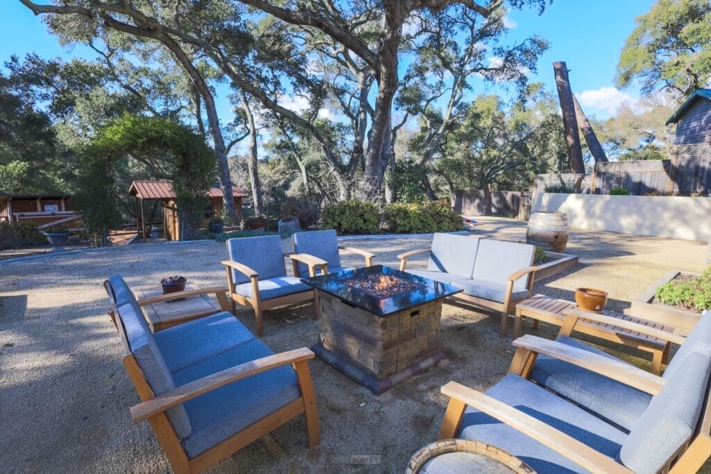 A vacation rental with a fire pit surrounded by chairs and trees, located in Pismo Beach on the Central Coast.