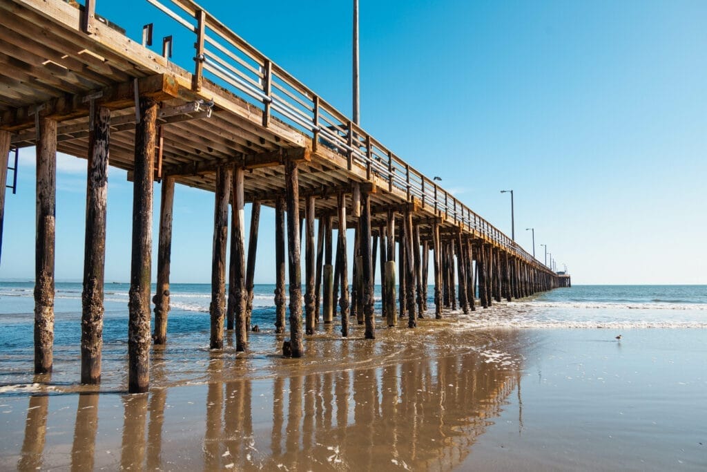 A pier with a lot of wooden poles in the water, located at Pismo Beach.
