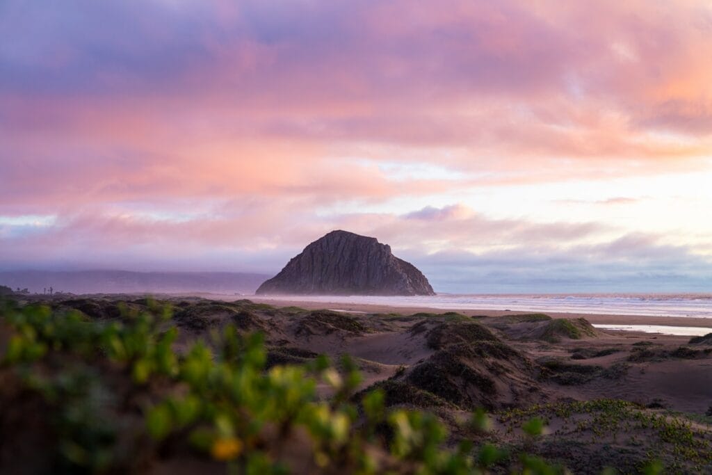A large rock on Morro Bay's sandy shore during sunset, perfect for a central coast vacation rental.